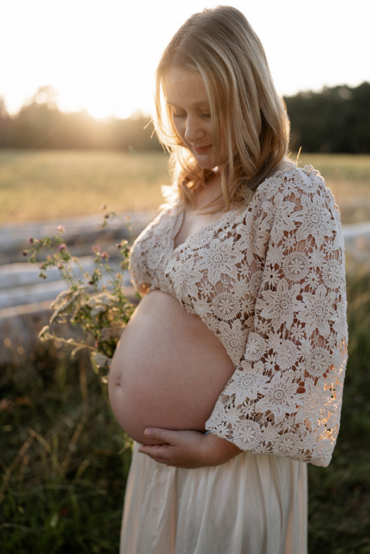 Schwangere im Spitzen-Top blickt lächelnd auf ihren Babybauch – Fotoshooting auf der Wiese in Lauchringen